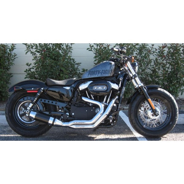 Black motorcycle parked on a street with a white wall and greenery in the background