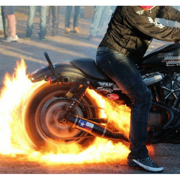 Person on a motorcycle with flames coming out of the exhaust, likely a Harley Davidson, on a street.