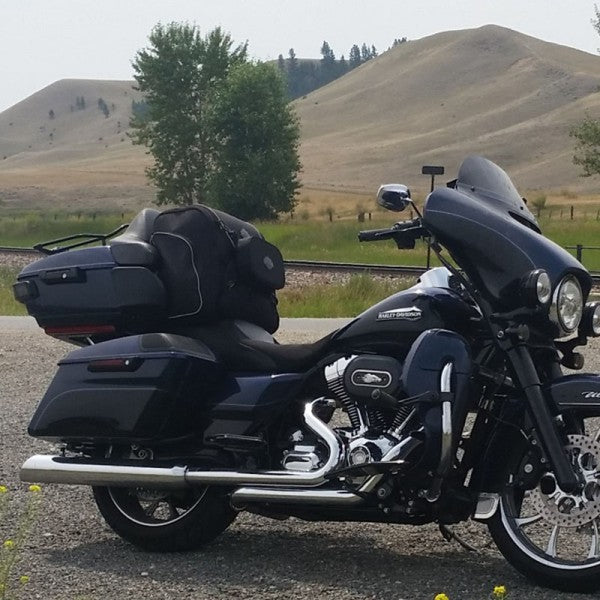 Black motorcycle with storage cases parked on a gravel road with hills and trees in the background