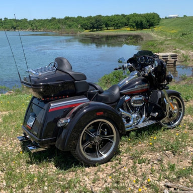 Black trike motorcycle parked by a lake with fishing rod on a grassy area