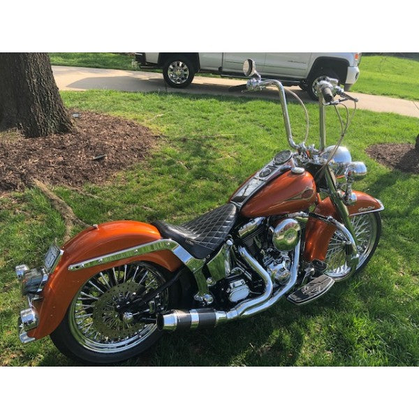 Orange motorcycle parked on grass with a tree and white vehicle in the background
