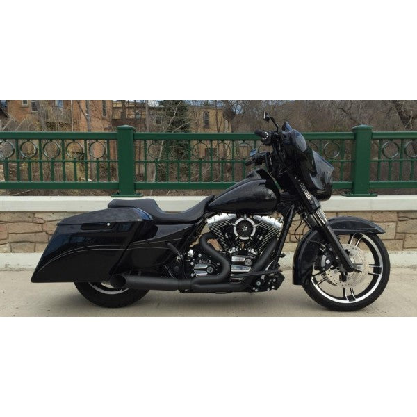 Black motorcycle parked on a sidewalk with a green fence and stone wall in the background