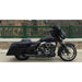 Black motorcycle parked on a sidewalk with a green fence and stone wall in the background